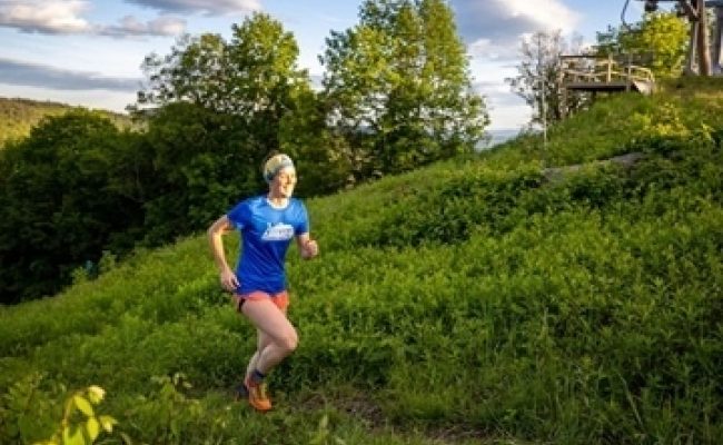 woman running up grassy hill blue tshirt top of ski lift in background